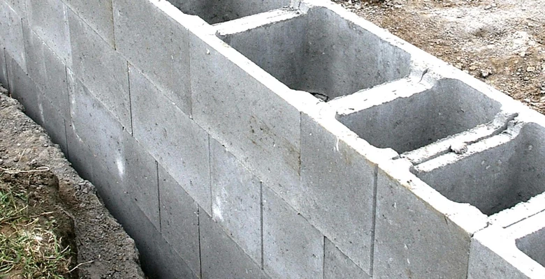 Stěna z betonových bloků s viditelnými prázdnými dutinami pro výztuž.