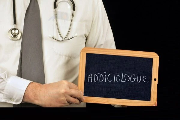 Doctor holding chalkboard with addictologue text