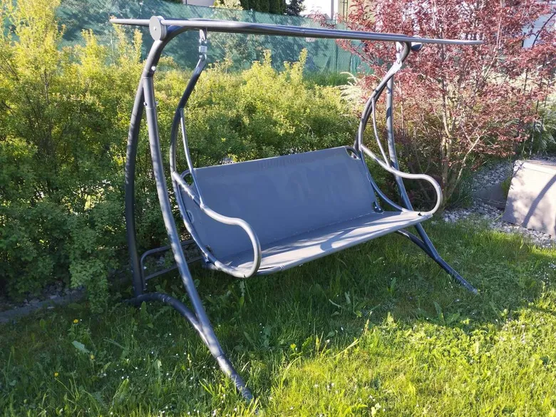 Houpací křeslo na zahradě s kovovým rámem a šedou látkovou sedačkou.