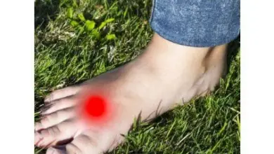 Bosá noha na trávě s červeným bodem ukazujícím bolest u Mortonova neuromu.