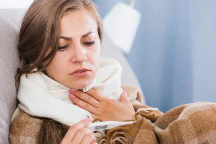 Žena s teploměrem a šátkem kolem krku při laryngitidě.