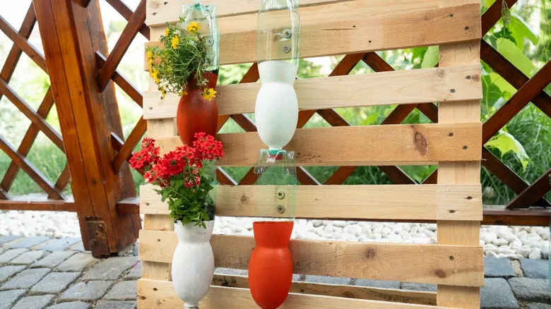 Svislá zahrada z palety s květinami v recyklovaných PET lahvích.