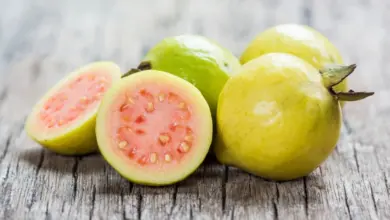 Čerstvé kvajávy nakrájené na polovinu a celé ležící na dřevě.
