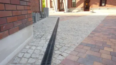 Černý odvodňovací žlab nainstalovaný vedle dlažby u cihlové zdi