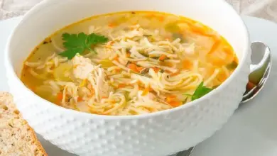 Mísa s kuřecím nudlovým polévku vedle kousku chleba.