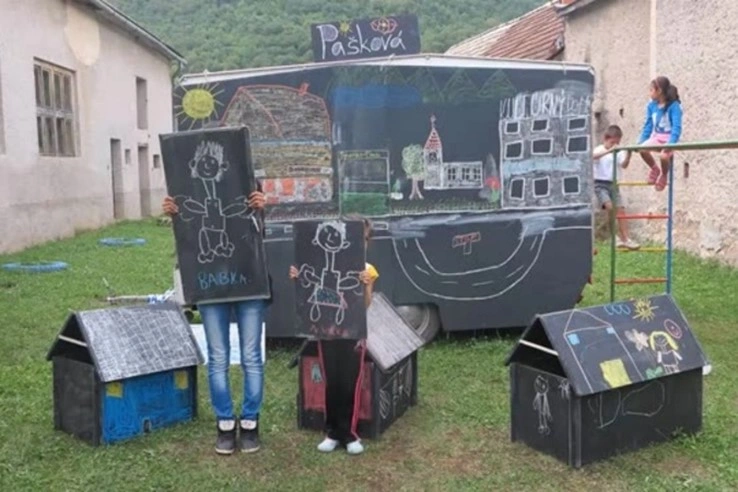 Děti kreslí lidi na tabulích vedle domků z kartonu.