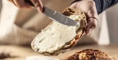 Rozmazávání bílého margarínu na kousku chleba nožem.