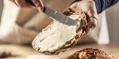 Rozmazávání bílého margarínu na kousku chleba nožem.