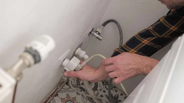 Ruční připojení vodovodních hadic k pračce během instalace.